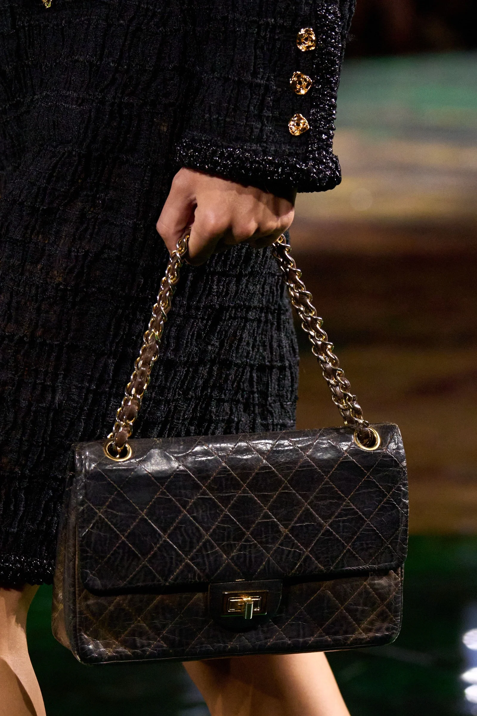 Closer: a black quilted leather flap bag held by its gold chain, worn and creased, with a rectangular turnlock.