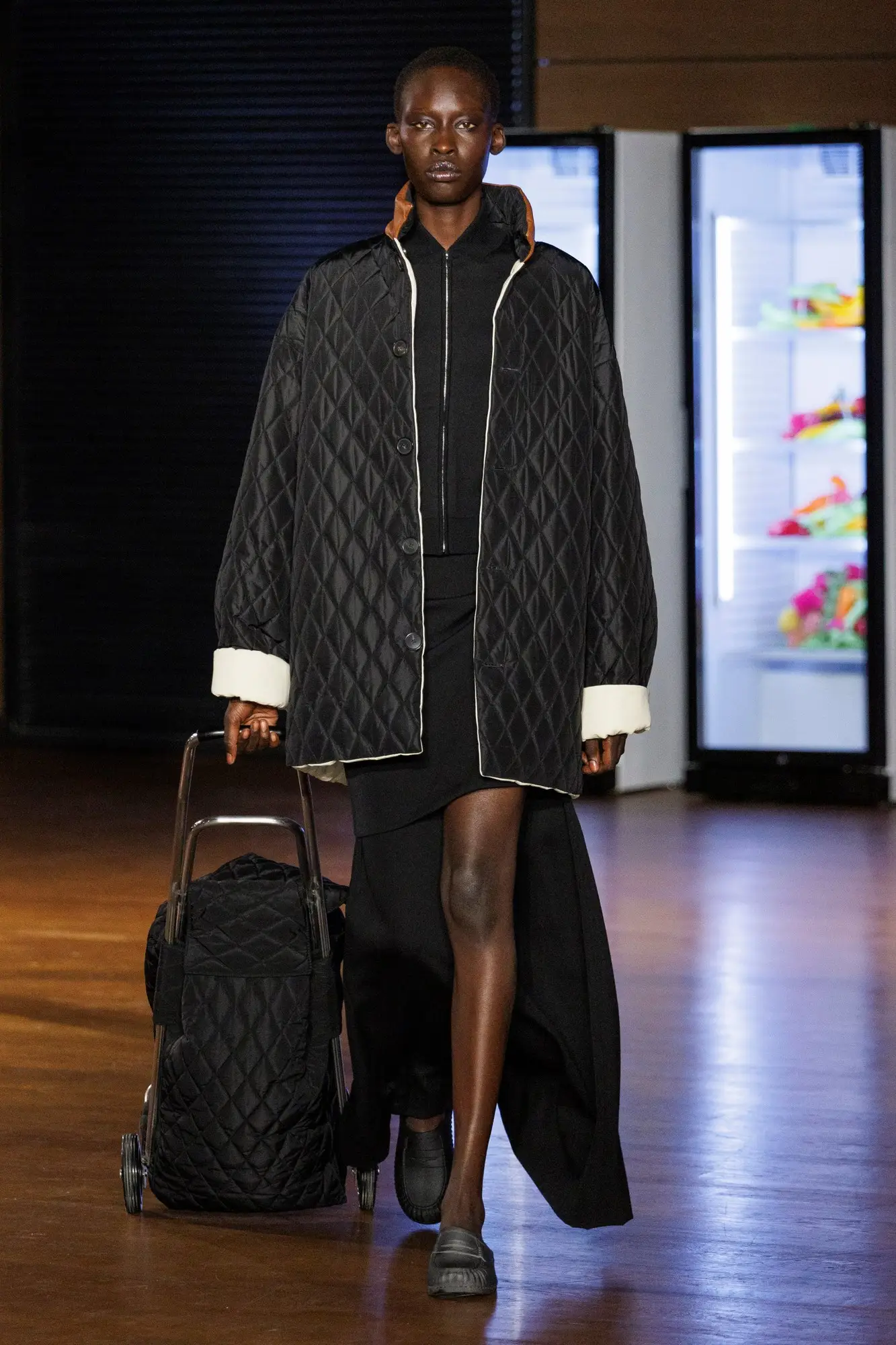 Look 29. Black quilted jacket, a black quilted trolley to match.