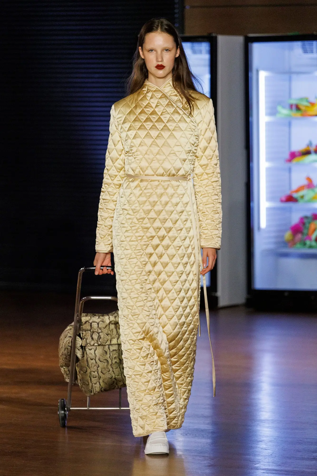 Marie Adam-Leenaerdt SS27, Look 38. A long quilted pale gold dress, full length, with a wheeled shopping trolley.