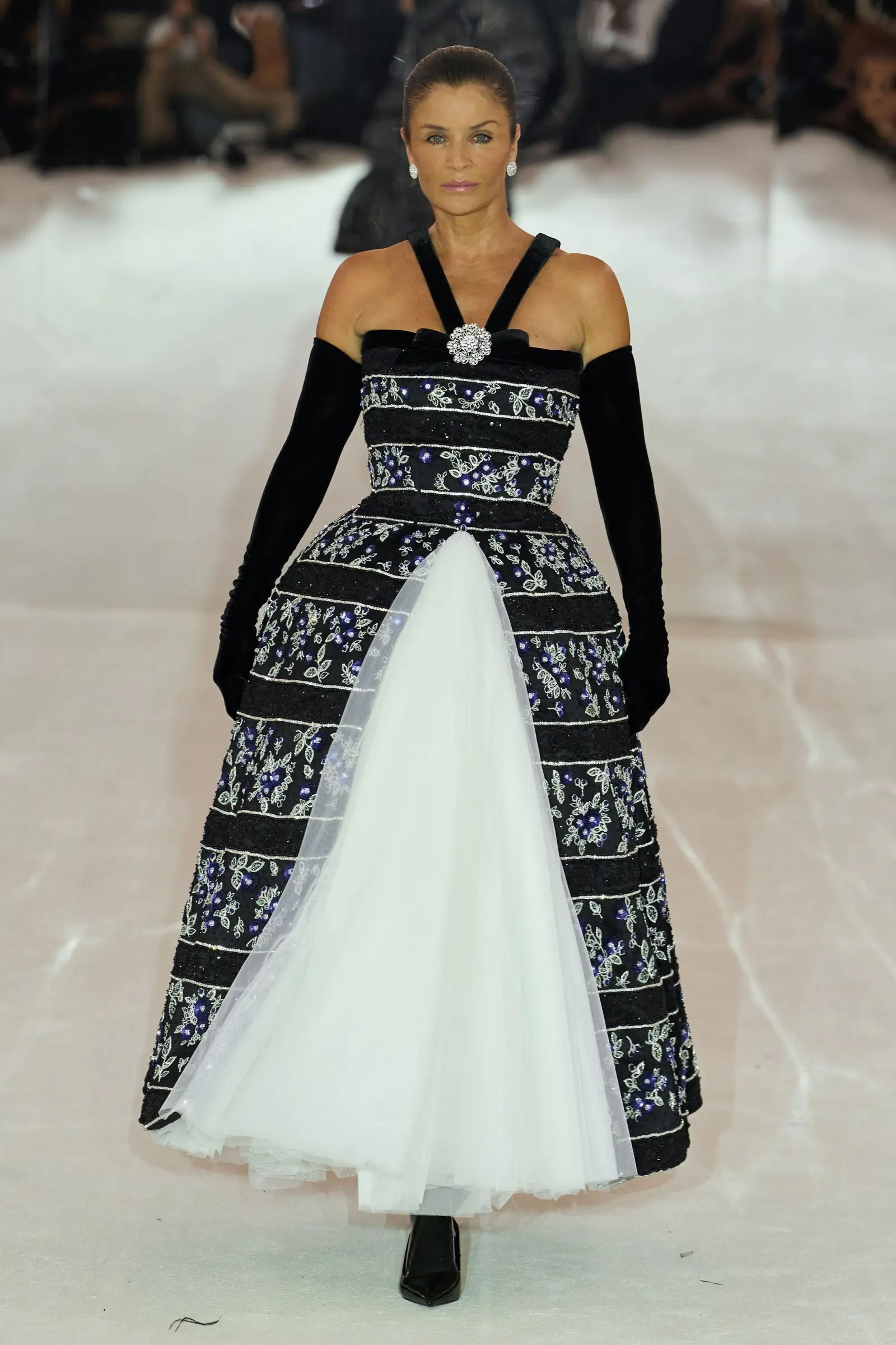 Richard Quinn SS27, Look 45. Helena Christensen in a navy and white embroidered gown with long black gloves.