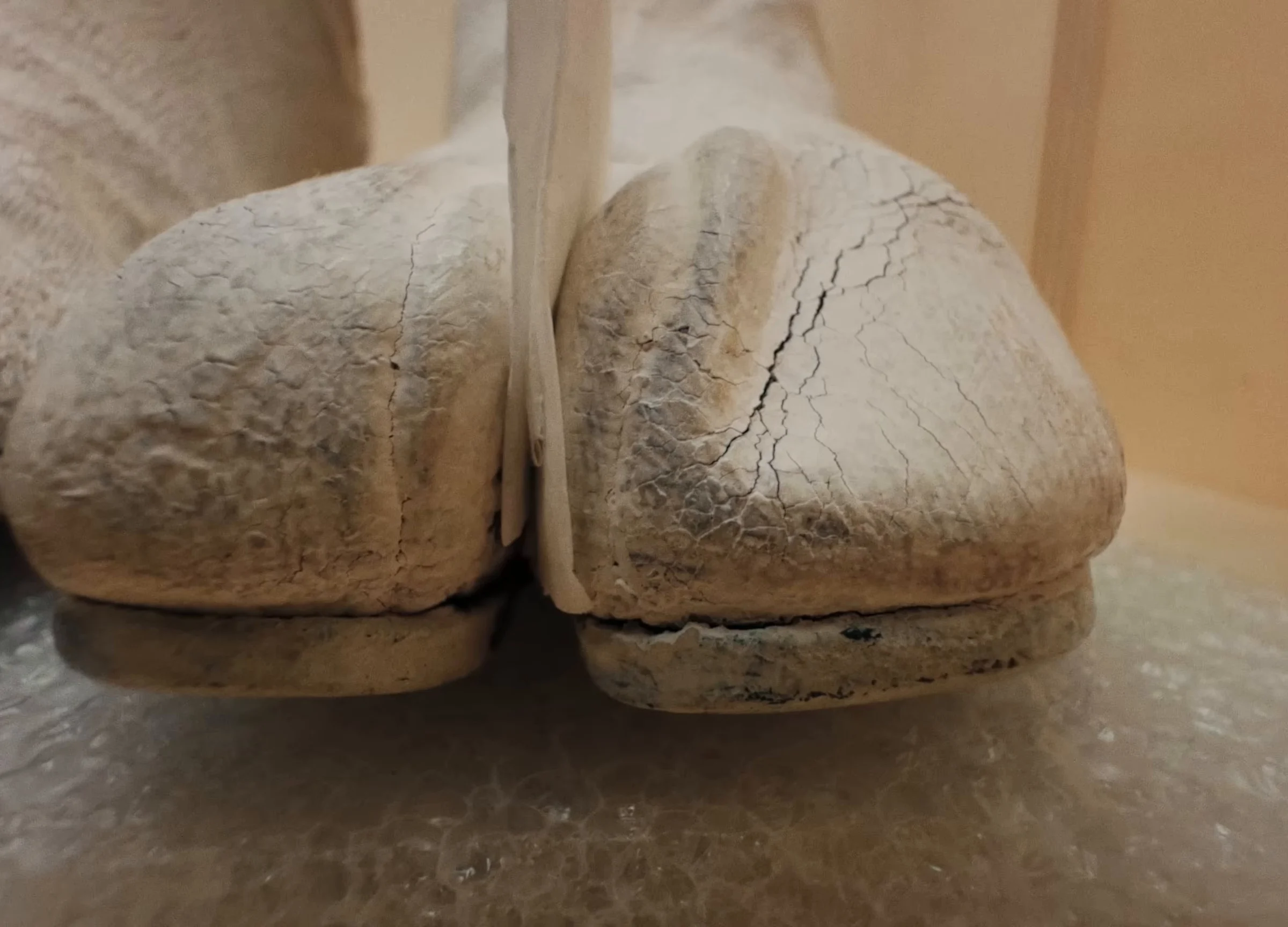 Closer, a second shot of the same pair: the front of one boot, the big toe split from the other toes, the white paint cracked across the leather.
